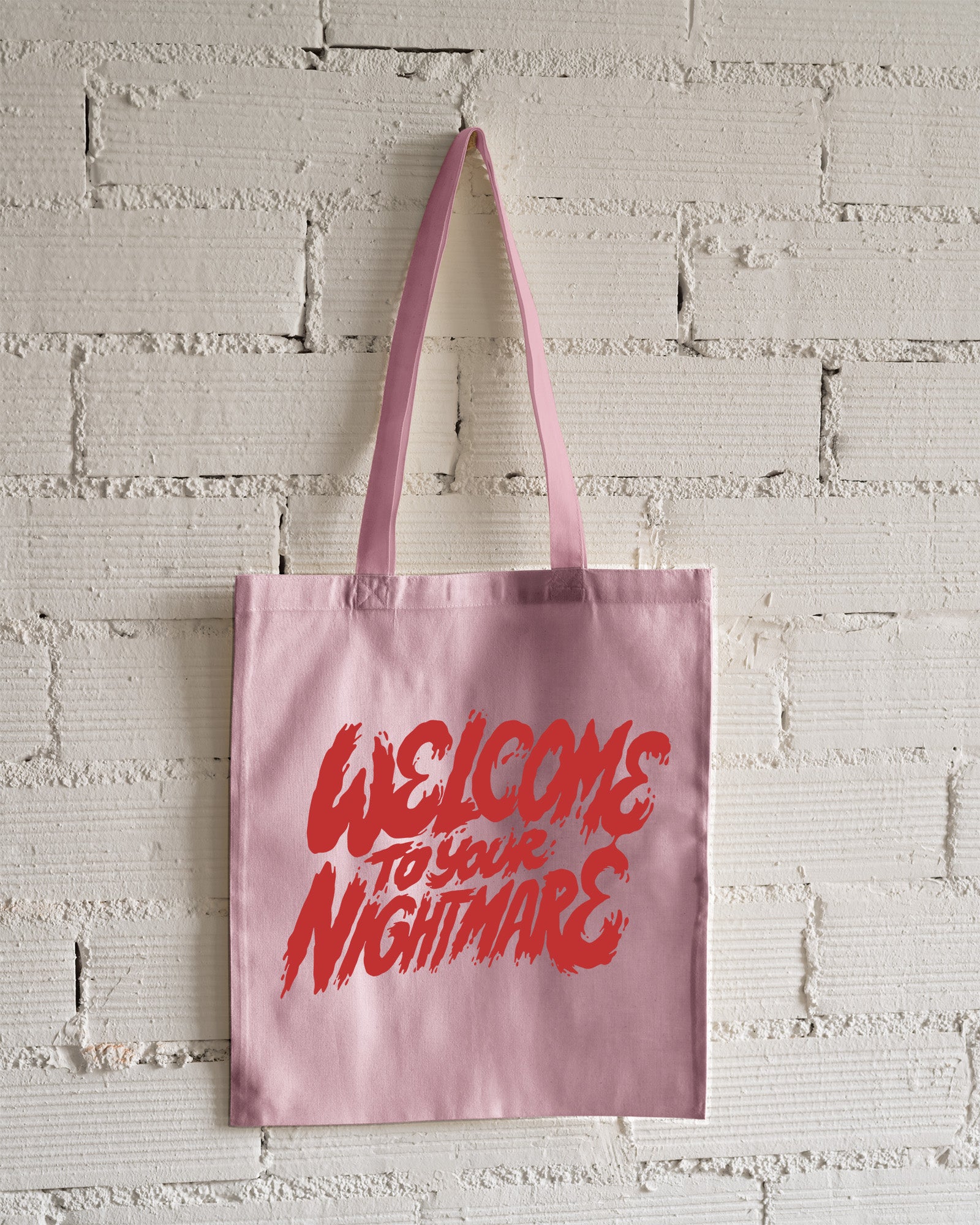 Pink tote bag featuring red text that reads Welcome to Your Nightmare in a horror-style font.