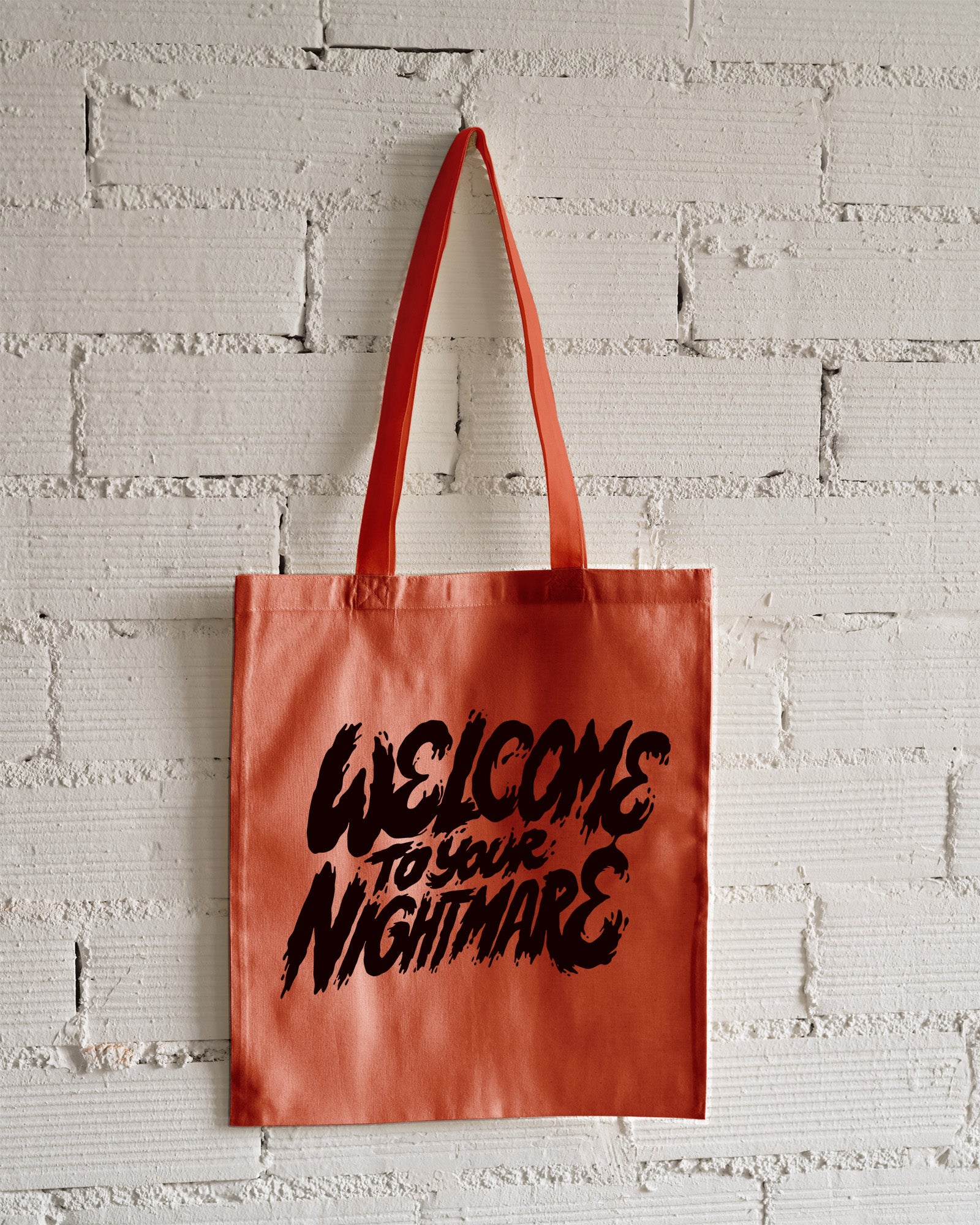 Orange tote bag featuring black text that reads Welcome to Your Nightmare in a horror-style font.