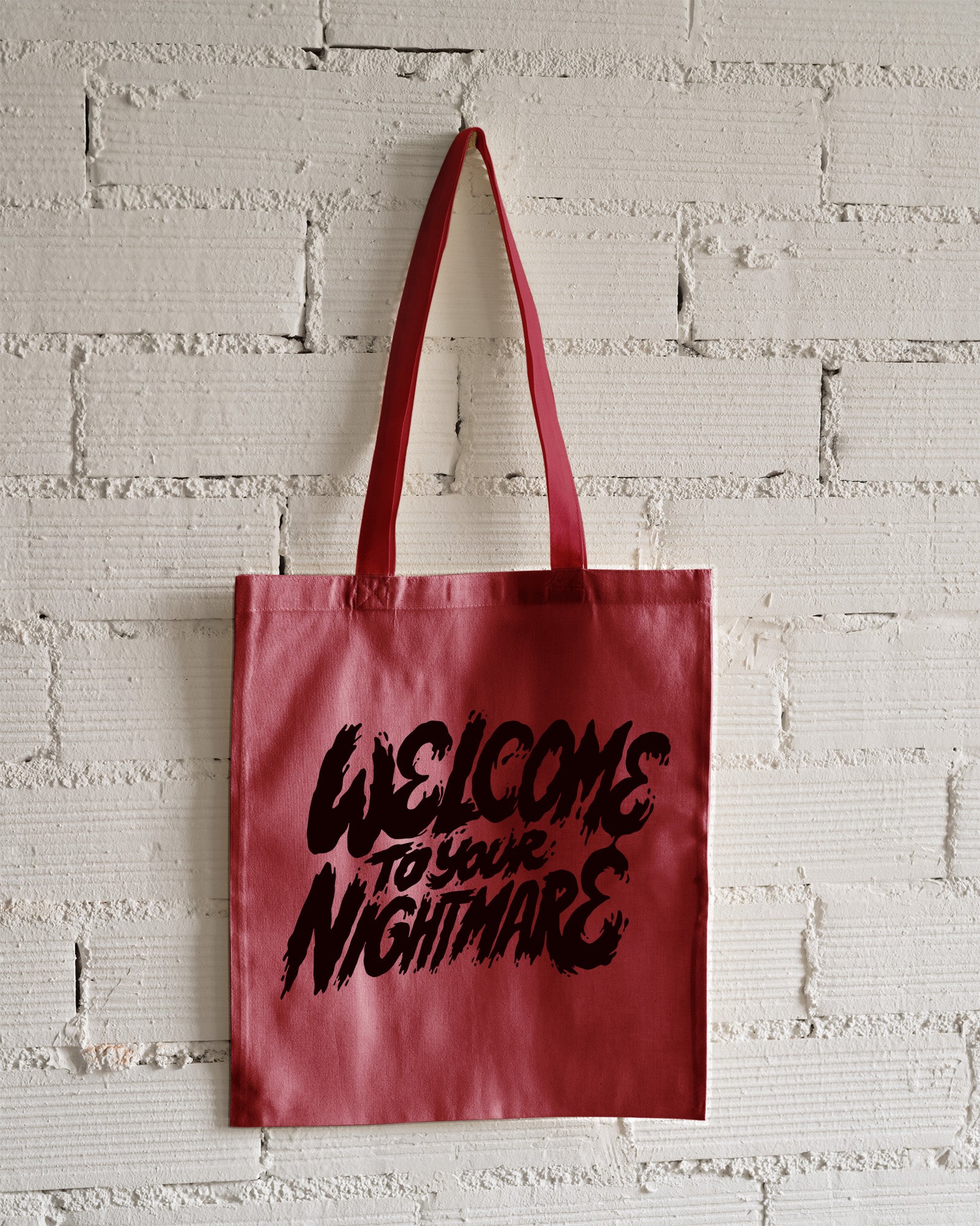 Red tote bag featuring black text that reads Welcome to Your Nightmare in a horror-style font.