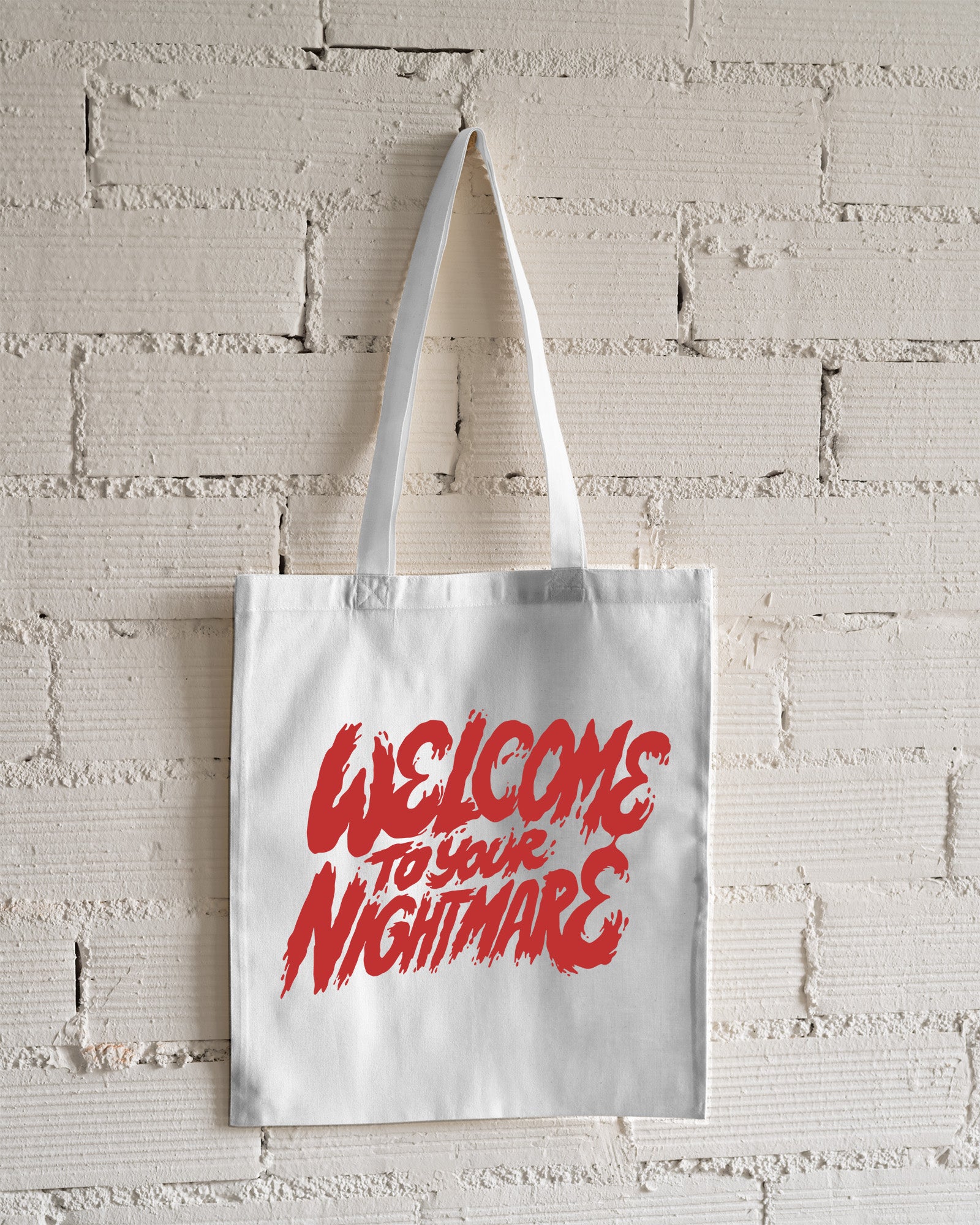 White tote bag featuring red text that reads Welcome to Your Nightmare in a horror-style font.