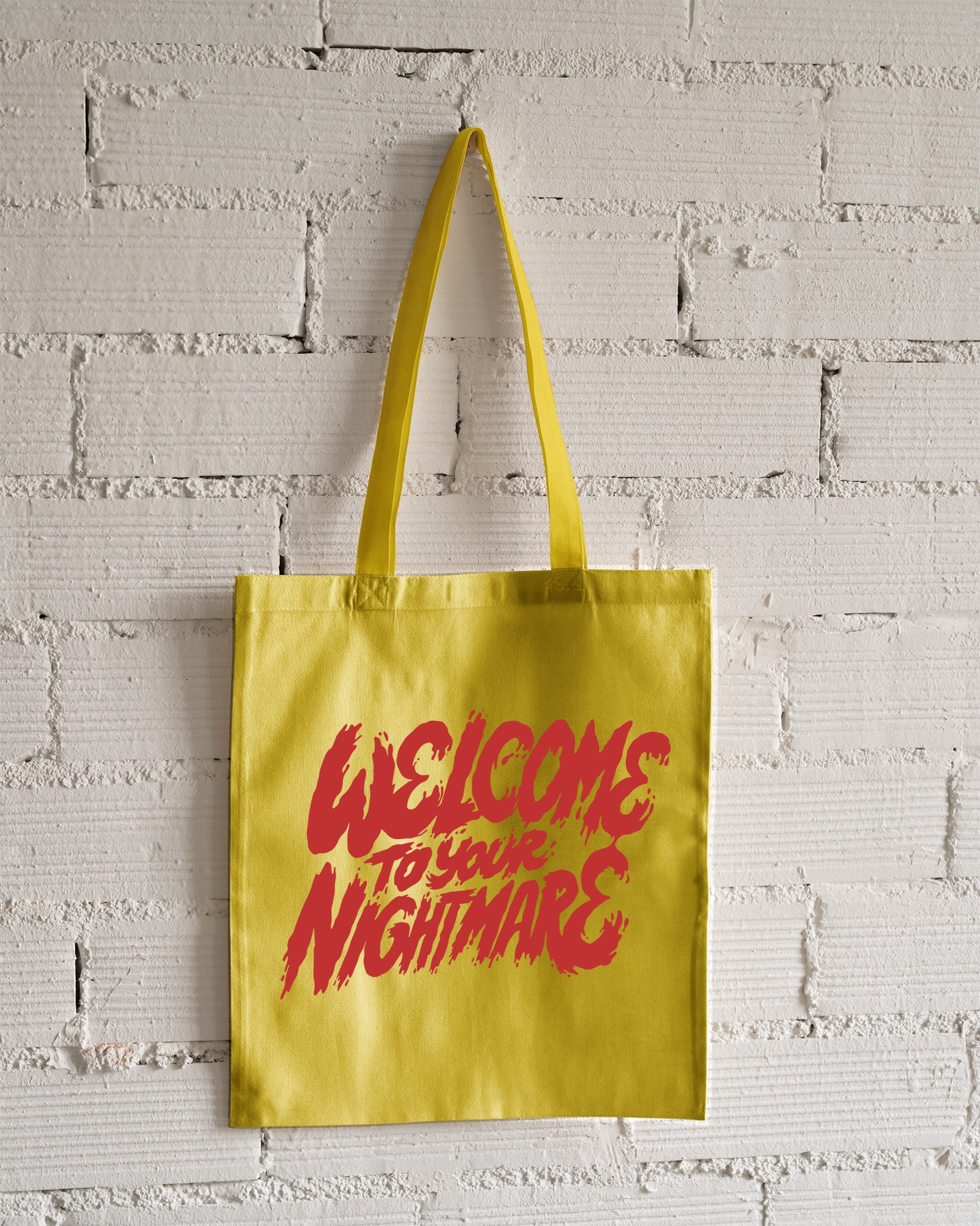White tote bag featuring red text that reads Welcome to Your Nightmare in a horror-style font.