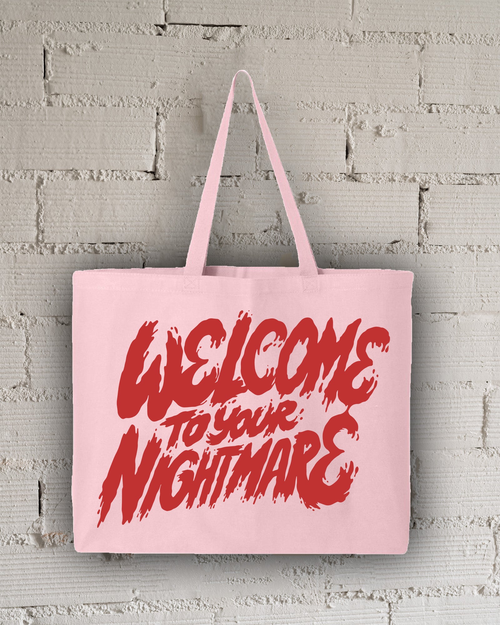 Pink tote bag featuring red text that reads Welcome to Your Nightmare in a horror-style font.